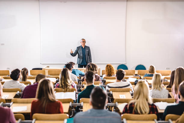 старший преподаватель разговаривает с большой группой студентов колледжа в амфитеатре. - adult classroom learning teacher стоковые фото и изображения