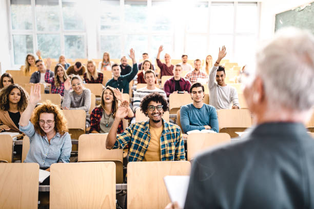 istock Large group of happy college students raising hands on a class. 1128725506