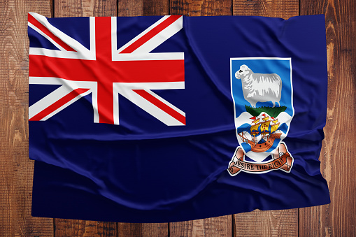Flag of Falkland Islands on a wooden table background. Wrinkled flag top view.