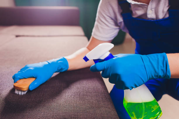 istock Cropped image. Cleaning concept. Male hand in light blue protective gloves cleaning sofa couch in the room. 1128740304
