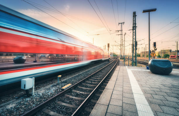 Red high speed train in motion on the railway station at colorful sunset. Blurred modern intercity train with sky reflection in windows on the railway platform. Passenger transportation. Railroad Red high speed train in motion on the railway station at colorful sunset. Blurred modern intercity train with sky reflection in windows on the railway platform. Passenger transportation. Railroad intercity train photos stock pictures, royalty-free photos & images