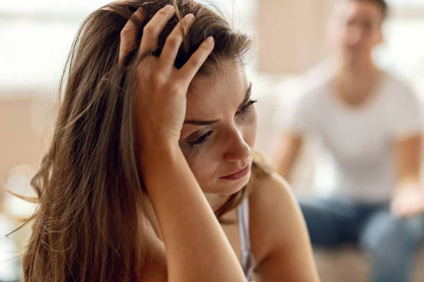 Heartbroken woman crying because of relationship problems she has. Young depressed woman having a headache and thinking while having relationship difficulties. Her boyfriend is in the background. woman mascara smudged stock pictures, royalty-free photos & images