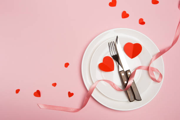istock Festive table setting for Valentine's Day with fork, knife,  hearts on a red background. Top view. - Image 1128742335