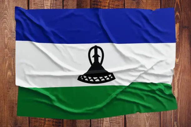 Photo of Flag of Lesotho on a wooden table background. Wrinkled Mosotho flag top view.