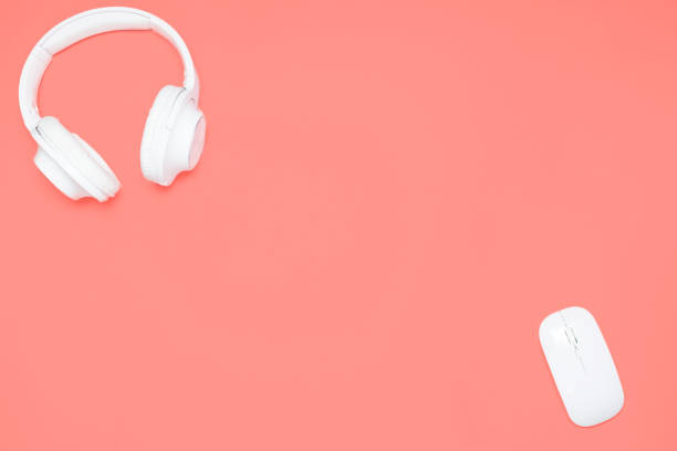 istock White Wireless headphones and wireless mouse on coral colored background. Top view. Flat lay 1128744814