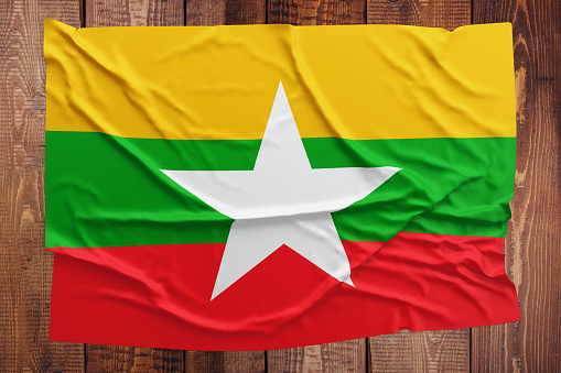 Flag of Myanmar - Burma on a wooden table background. Wrinkled Burmese flag top view.