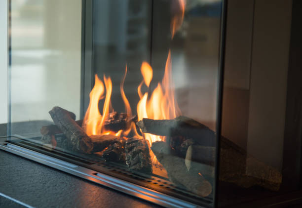 a fire burns in a glass fireplace, radiates heat - fire place imagens e fotografias de stock