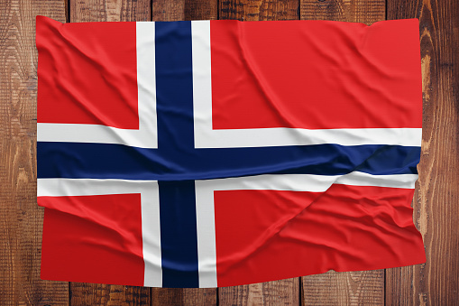 Flag of Norway on a wooden table background. Wrinkled Norwegian flag top view.