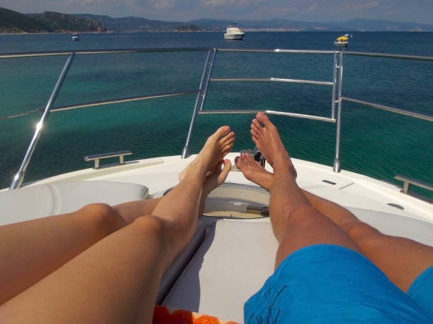 istock Legs laying on white luxury yacht with background beautiful multicolor sea with 2 small yachts on horizon. Luxury relaxation vacation theme 1128747498