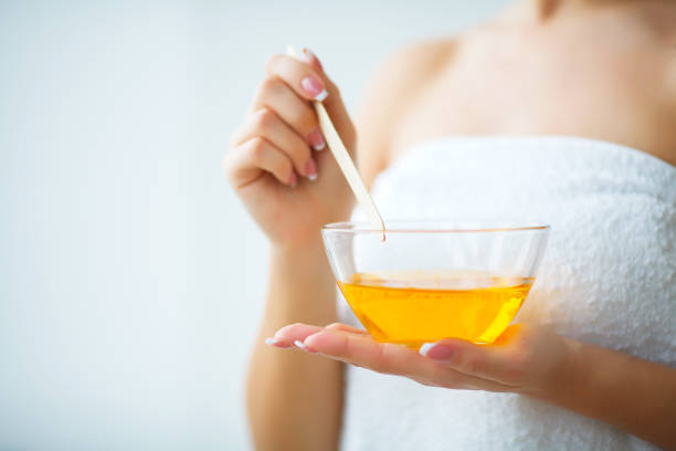istock Female hand and orange paraffin wax in bowl. 1128748209