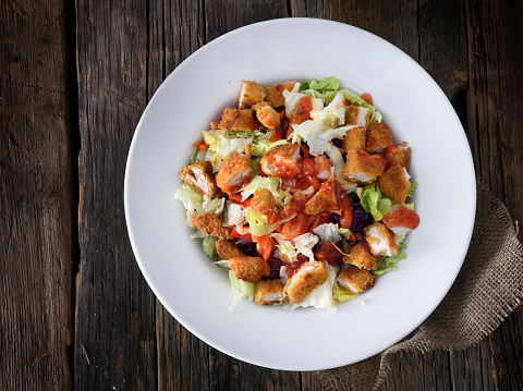 Crispy fried chicken salad with thai sauce, red bell pepper and red cabbage on a wooden background