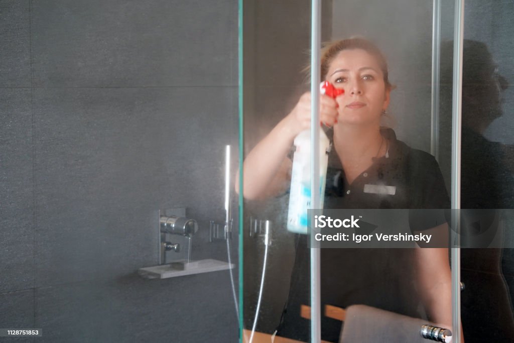 Woman housekeeper cleaner in the bathroom The maid in the bathroom wipes the glass of the shower room in the hotel room. Cleaning. Woman cleans the glass in the bathroom 30-39 Years Stock Photo