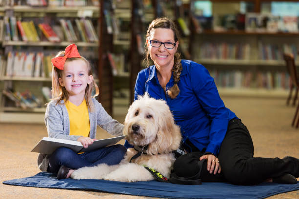 istock Girl in library reading with therapy dog and trainer 1128755728