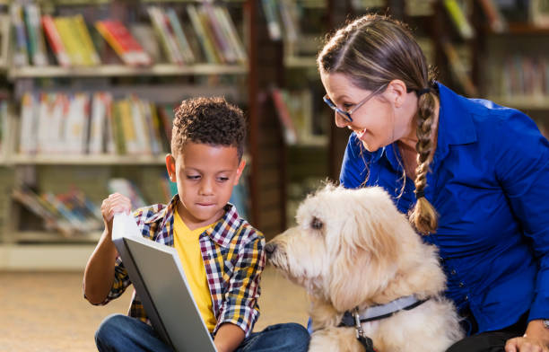 istock Mixed race boy reading in library with therapy dog 1128755978