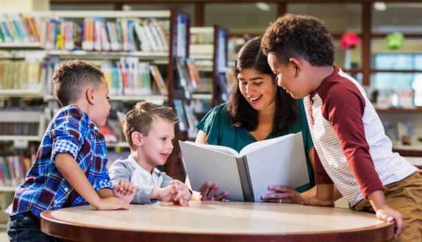 istock Hispanic teacher with three boys in library reading book 1128757010