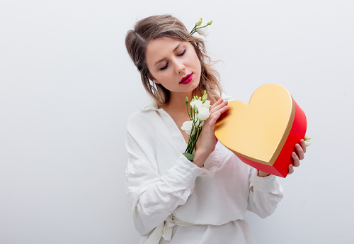 Beautiful woman with white roses dressing in a white shirt holding a heart shape gift box. Springtime concept or Valentines Day holiday