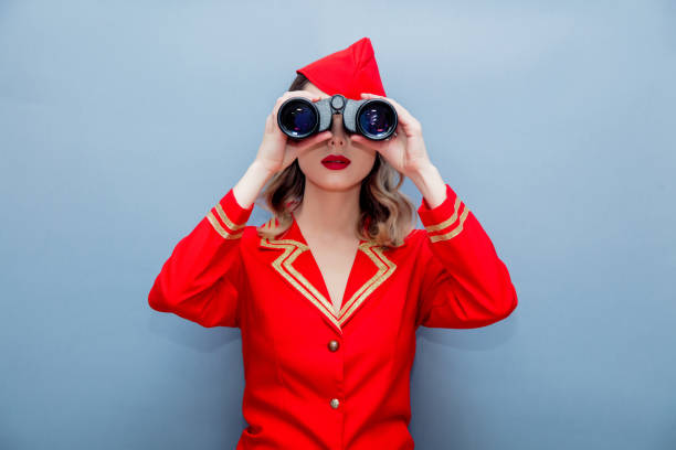 Portrait of charming vintage stewardess wearing in red uniform with binoculars. Isolated on gray background.