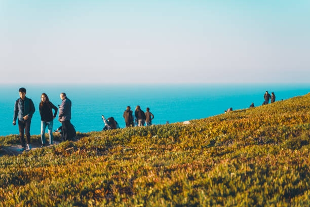 menschen am rande europas bei sonnenuntergang, kap roca - cliff at the edge of grass sea stock-fotos und bilder