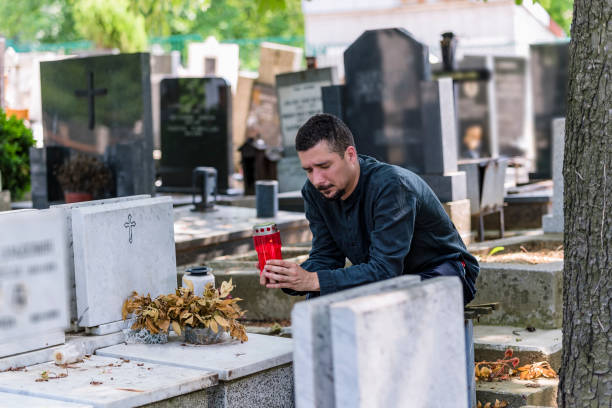 istock Man Sitting At Grave Sites with Red Candle 1128780658