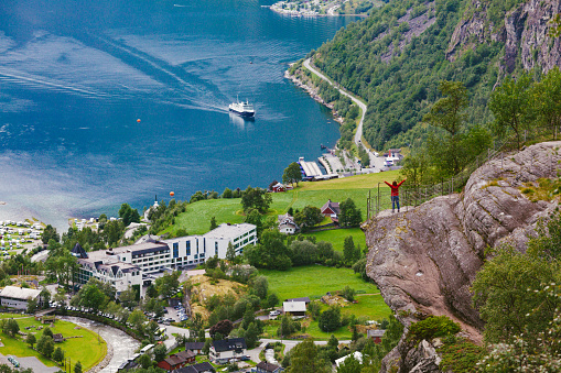 Tiny figure of tourist on the rock over the green Gerainger fjord coastline with its hotel and cottages.