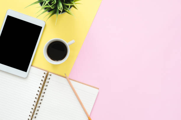 istock Office desk working space - Flat lay top view photo of working space with blank mock up tablet, coffee cup and notebook on pastel background. Pastel pink yellow color copy space working desk concept. 1128781270