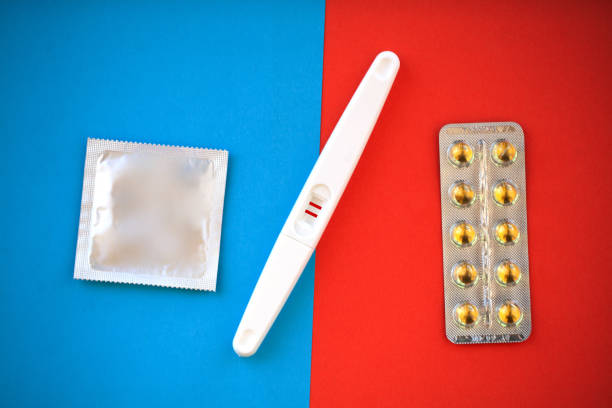 test de grossesse. le résultat est positif avec deux bandes et préservatif avec contraceptif sur fond coloré, pilule contraceptive, safe sex, concept de soins de santé - contraceptive sex education birth control pill condom photos et images de collection