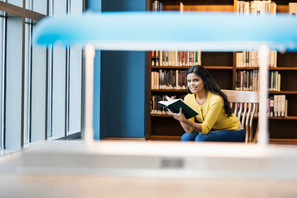 istock Young Hispanic woman in library reading book 1128814837