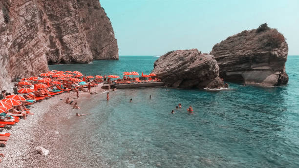 istock Panoramic view of pebble beach with clear azure blue water, layered rocks and red beach umbrellas, beautiful mediterranean Adriatic Sea coast, Montenegro. 1128817014