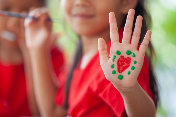 istock Child drawing and painting a heart on her hand with fun 1128820636