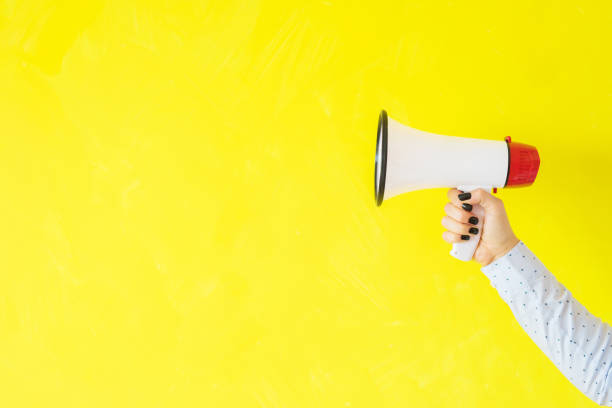 istock Person holding megaphone on empty yellow background 1128821707