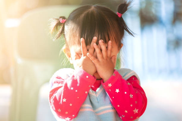 Cute asian baby girl closing her face and playing peekaboo or hide and seek stock photo