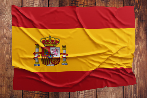 Flag of Spain on a wooden table background. Wrinkled Spanish flag top view.