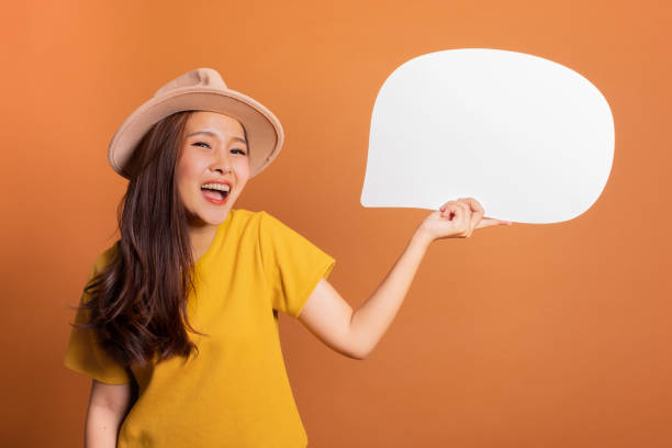 istock Young Asian woman show text box, speech bubble and copy space over orange background, empty space for text and ads, studio light 1128833668