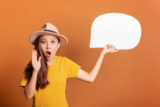Young Asian woman show text box, speech bubble and copy space over orange background, empty space for text and ads, studio light