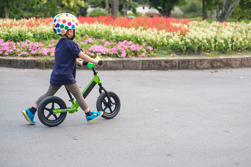 Cute little 2 - 3 years old toddler boy child wearing safety helmet learning to ride first balance bike in sunny summer day, kid cycling at park, Explore & Appreciate Nature with toddlers concept