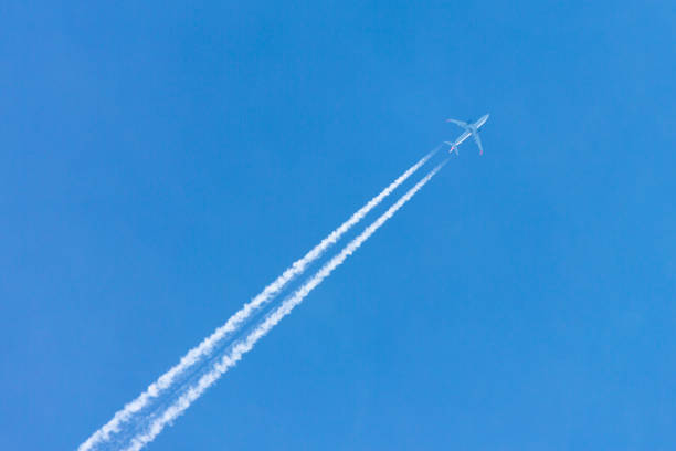 Plane flying high in clear blue sky leaving long white trail.