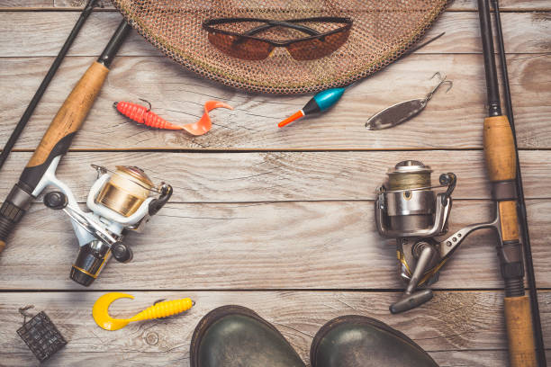 Fishing background theme. Fishing rods with reels, fishing tackles, rubber boots, fishing buoy and polarized glasses on greywooden background with copy space Fishing background theme. Fishing rods with reels, fishing tackles, rubber boots, fishing buoy and polarized glasses on greywooden background with copy space. minnow fish photos stock pictures, royalty-free photos & images
