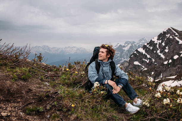 istock excited young handsome hiker sitting on the hill with flowers 1128852371