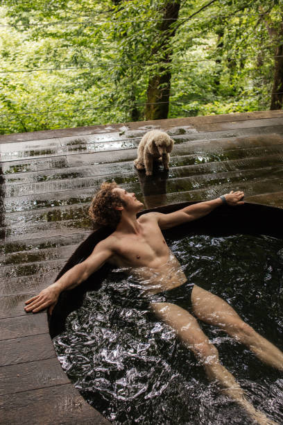 istock positive, cheerful man is looking at his dog while lying on the bathtub 1128853346