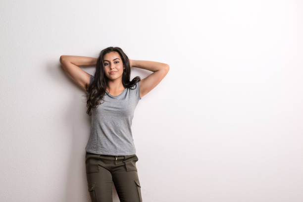 Young beautiful happy woman standing in a studio in studio, hands behind her head.