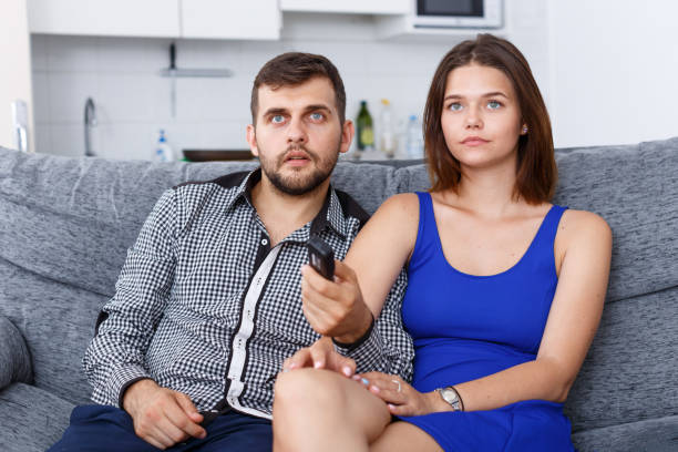 istock Smiling young couple sitting on sofa at home watching TV 1128856877