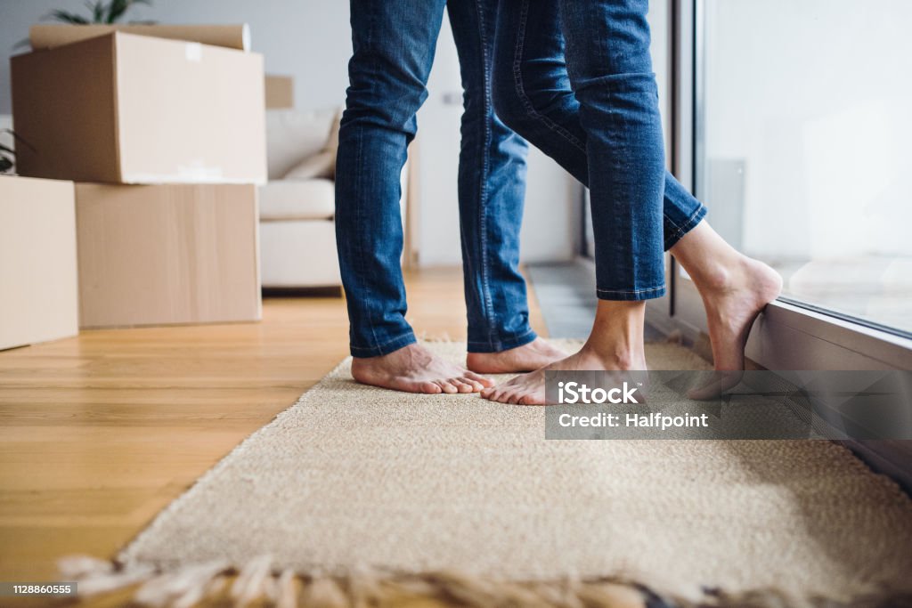 A midsection of young couple moving in a new home, standing by a window. A midsection of legs and feet of young couple moving in a new home, standing by a window. Men Stock Photo