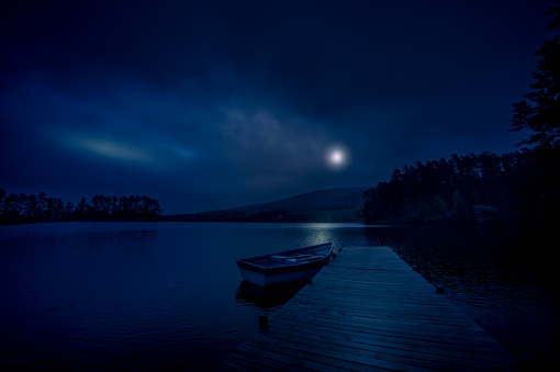 Full Moon reflections on jetty and lake with moored rowboat