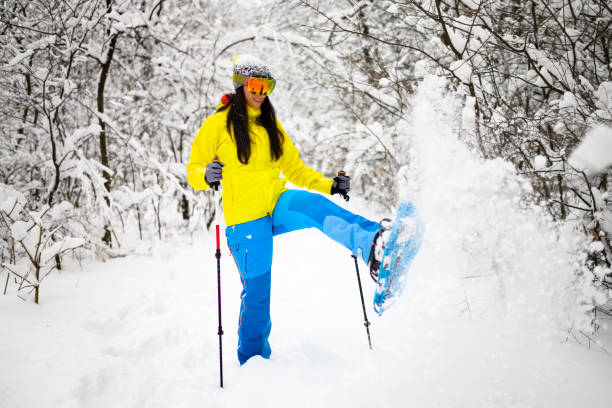 Close-up view beautiful young woman in winter clothes stands sideways and holds sticks in hand on a background the snow mountain