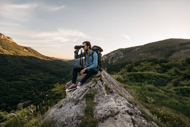 excursionista sentada sobre la roca mirando a través de binoculares - mirar a través fotografías e imágenes de stock