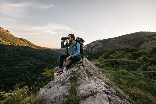 Hiker sitting on rock looking through binoculars