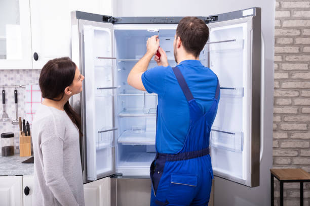 Repairman Fixing Refrigerator With Screwdriver Woman Looking At Male Repairman Fixing Refrigerator With Screwdriver fridge problem stock pictures, royalty-free photos & images