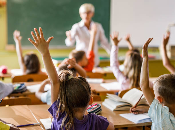 istock Back view of a school kids raising their hands on a class in the classroom. 1128874876