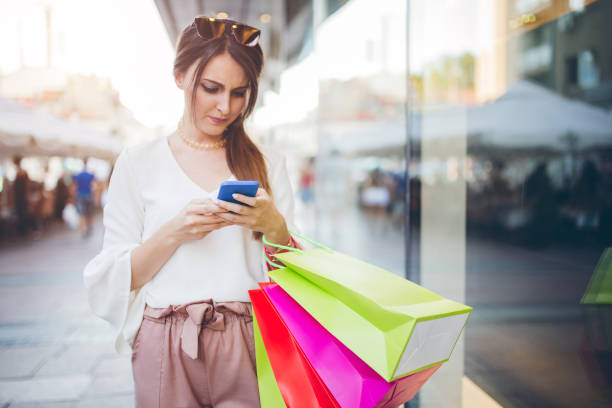 istock Young woman with shopping bags using smartphone. 1128879546