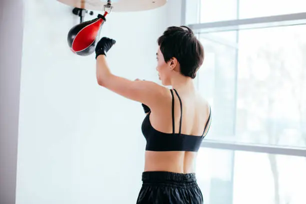 rear view image of fit woman performing kicks on speed bag at fitness studio. deliver a thrust. concept of sportswoman's life